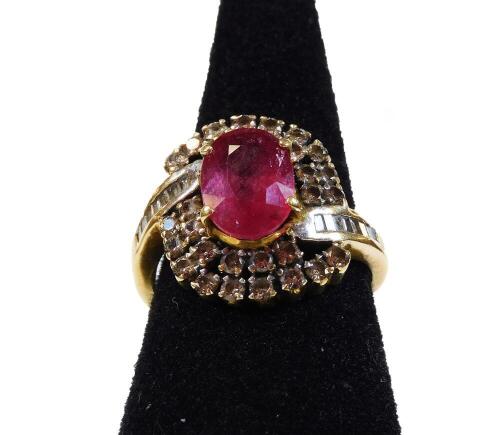 A ruby and diamond dress ring, with central oval cut ruby, in four claw setting, surrounded by two rows of round brilliant diamonds, and with baguette cut diamond shoulders, in a twist design, yellow metal, unmarked, tests as 18ct, ring size N½, 6.4g all