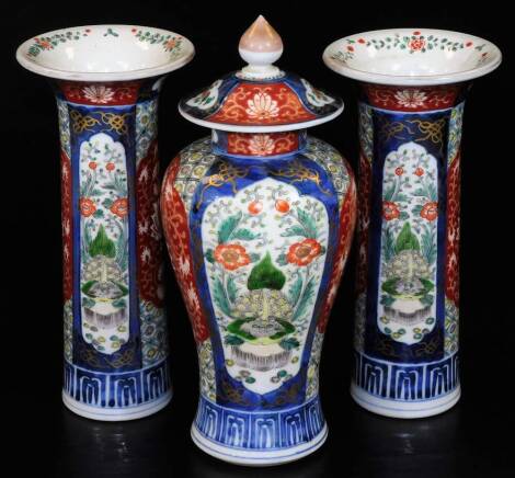 A Japaneseiece three piece Imari garniture comprising two trumpet cases and a lidded baluster jar, decorated with panels of shish among flowers, predominately in orange and blue with gilt highlights, 27cm H. (3,1 AF)