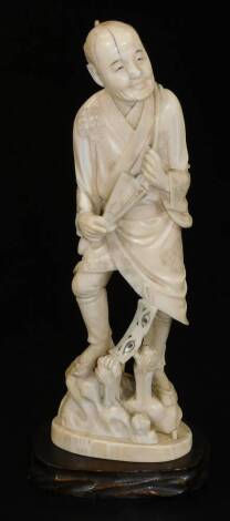 A Japanese Meiji period ivory okimono figure, of a man in robes holding fan, standing on a rocky outcrop, signed on the underside, wood stand, the figure 22cm H.