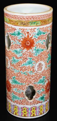 A 20thC Chinese porcelain spill vase, of cylindrical form pierced with shaped cutouts, decorated with scrolling peony designs around long life characters in orange and green between key fret and lappet borders. Six character Qianlong mark in red to the ba