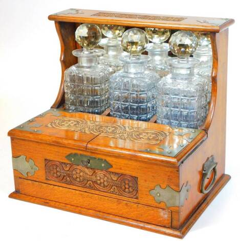 An early Edwardian oak three bottled tantalus, in heavily carved oak case, with metal mounts and front opening, set with three cut glass bottles, with front drawer and elaborate escutcheon, 33cm H, 35cm W, 26cm D.