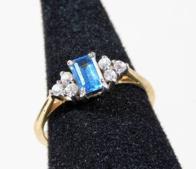 A 9ct gold dress ring, with central rectangular cut blue topaz stone, flanked by three white stones to each side, in a raised basket setting, ring size P, 2.4g all in.