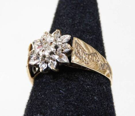 A 9ct gold dress ring, with central flower design, set with illusion set white stones, with etched and bark style shoulders, ring size Q½, 2.9g all in.