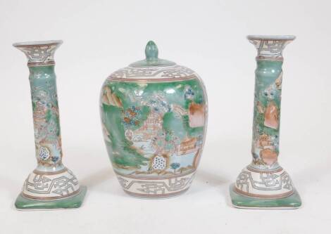 Various 20thC Chinese pottery, comprising a pair of candlesticks and lidded jar, each decorated with scenes of buildings and flowers on a green ground with an upper geometric pattern to the jar, 23cm H. (3)