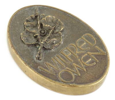 A bronze plaque or paperweight, dedicated to the war poet Wilfred Owen (1893-1918), cast with a poppy to one side, the reverse stating The Poetry is in the Pity, with various notes to the border.