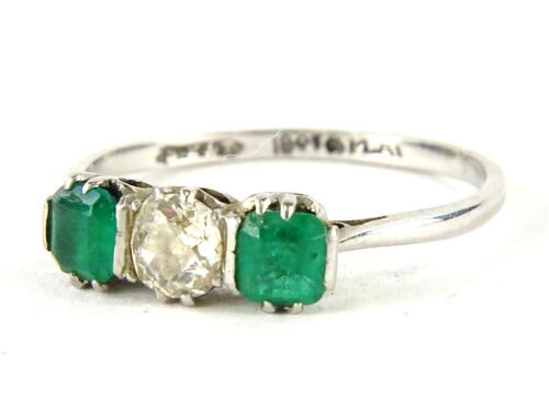 An emerald and diamond three stone ring, with central old cut diamond, measuring 4.8mm x 4.8mm x 2.4mm, approx 0.35cts, flanked by two rectangle cut emeralds, each approx 4.2mm x 3.4mm x 2.2mm, in raised claw basket setting, white metal, marked 18ct and p