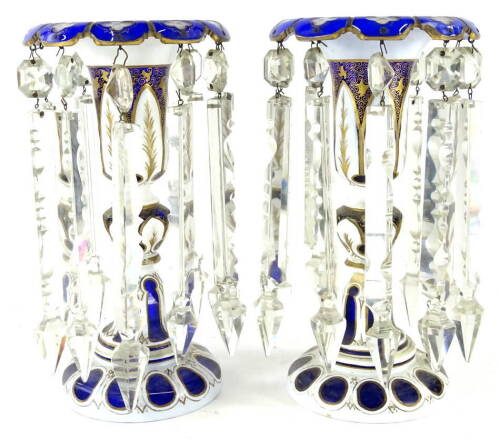 A pair of 19thC Bohemian blue, clear and milk glass lustres, each with floral tops and inverted stems, with gilt highlights set with flowers, on circular feet, with cut glass droppers, 28cm high.