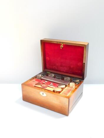 A Victorian rosewood travelling box with mother of pearl escutcheon, the hinged lid opening to reveal a fitted interior, with cut glass bottles and jars with cut glass stoppers or plated lids, together with a manicure set, to the side a semi secret drawer