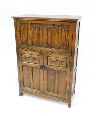 An Old Charm oak drinks cabinet, with cantilever fall front and top, with linen fold panels, the cupboard below enclosed by two panelled and arcaded doors, 109cm H, 76cm W.