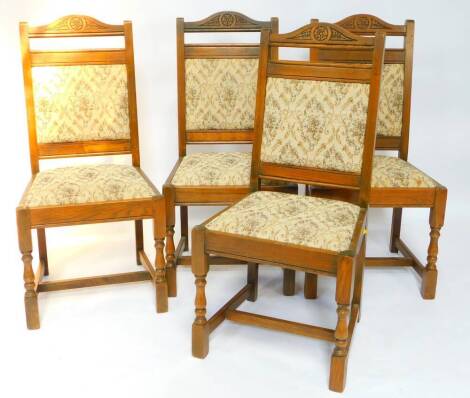 A set of four Old Charm oak single dining chairs, with floral carved crest rails, floral tapestry style overstuffed backs and drop in seats, raised on turned legs united by an H framed stretcher.