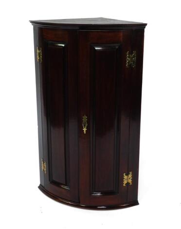 A George III mahogany bowfronted hanging corner cupboard, with two doors opening to reveal three shelves, raised on a plinth base, 56cm W, 39cm D, 89cm H.