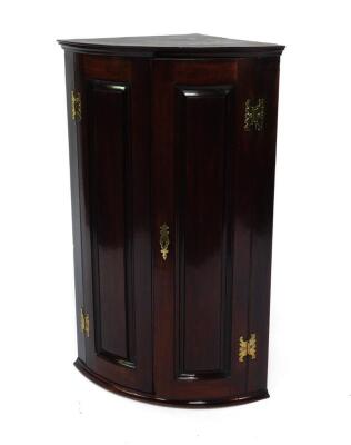 A George III mahogany bowfronted hanging corner cupboard, with two doors opening to reveal three shelves, raised on a plinth base, 56cm W, 39cm D, 89cm H.