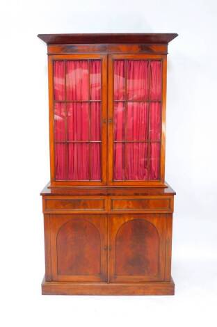 A Victorian flame mahogany cupboard bookcase, the outside pediment over two glazed doors, opening to reveal three height adjustable shelves, over two cushion drawers above panelled doors, opened to reveal a further shelf, raised on a plinth base, 109.5cm 