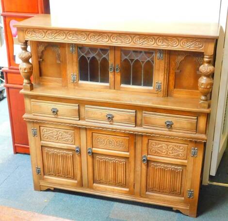 An Elizabethan style oak court cupboard, with carved S scroll top frieze, raised on leaf carved cup and cover turned supports, with a pair of glazed doors, flanked by carved panel sections, over three drawers above linen fold panel cupboard doors, with le