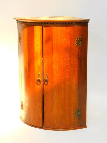 An oak Georgian style bow fronted hanging corner cupboard, the dentil moulded pediment over two doors opening to reveal two shelves on a plinth base, 87cm H, 65.5cm W, 47cm D.