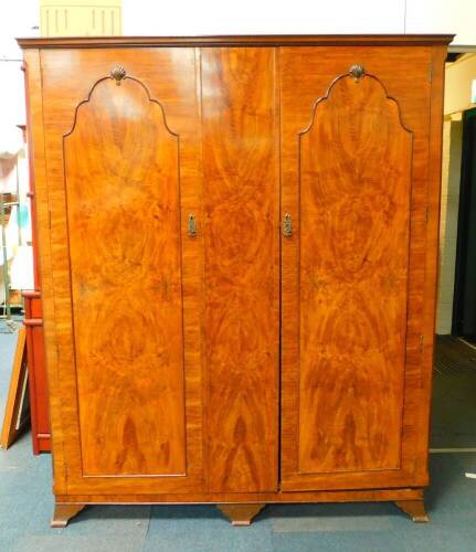 An early 20thC walnut and mahogany compactum wardrobe, the outswept pediment over two doors, flanking a centre panel opening to reveal a double hanging space, flanked by five shelves, raised on bracket feet, 191.5cm H, 157cm W, 56.5cm D.