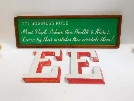 A pair of pottery E wall plaques, 34cm x 24.5cm, together with a framed tin sign, painted with 'No 1 Business Rule; Meet People, Admire Their Wealth And Wares, Learn By Their Mistakes Then Overtake Them!, 28cm x 94cm. (3)