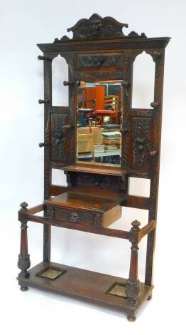 A Victorian oak mirror back hall stand, the arched pediment carved with a lion's head mask, the rectangular bevel glass mirror in a surround of recesses and panels carved with fruit and acanthus leaves, above a shelf and frieze drawer, flanked by two rece