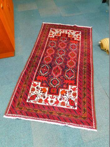 A Qum wool rug, decorated with fourteen guls, four fish, flowers and a vase and birds, within a triple geometric border, against a white, blue and red ground, 189cm x 104cm.