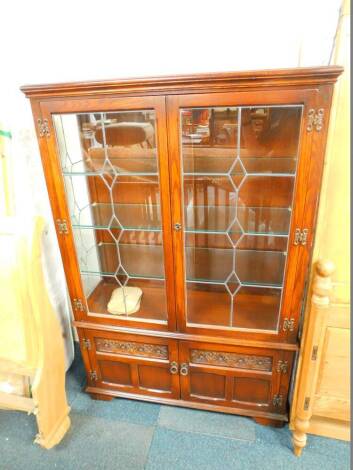 An Old Charm oak display cabinet, the outset pediment over two glazed doors opening to reveal three glass shelves and glazed sides, over a pair of carved panel doors, raised on bracket feet, 160.5cm high, 117cm wide, 39cm deep.