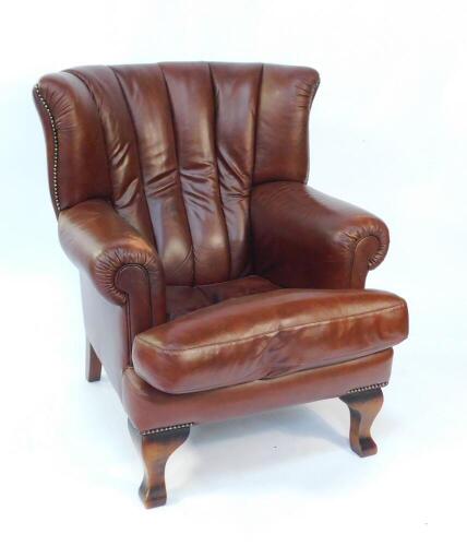 A tan leather wing armchair, with loose cushion seat, raised on mahogany cabriole legs, 105.5cm high, 82cm wide. The upholstery in this lot does not comply with the 1988 (Fire & Fire Furnishing) Regulations, unless sold to a known exporter or upholsterer