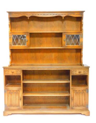 An Old Charm style oak dresser, the outswept pediment over a two shelf plate rack, with glazed cupboards, over three central shelves, flanked by two drawers, recesses and linenfold cupboard doors, raised on a bracket foot base, 183cn H, 149cm W, 26.5cm D