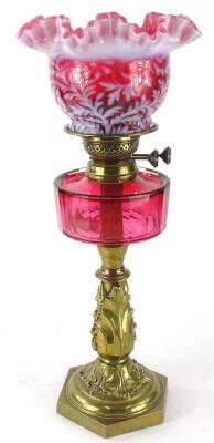 A late Victorian cranberry and brass oil lamp, with shaped floral milk glass shade, set with flowers with handkerchief top, on a pierced brass stand, marked Duplex, with a cranberry glass reservoir on an acanthus leaf stem and hexagonal base, 51cm high.