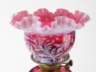 A late Victorian cranberry and brass oil lamp, with shaped floral milk glass shade, set with flowers with handkerchief top, on a pierced brass stand, marked Duplex, with a cranberry glass reservoir on an acanthus leaf stem and hexagonal base, 51cm high. - 2