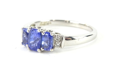 An 18ct white gold dress ring, claw set with three graduated bluey/purple stones, possibly tanzanite, flanked by small diamonds to the shoulder, on a part pierced shank, size O, 3.5g all in.