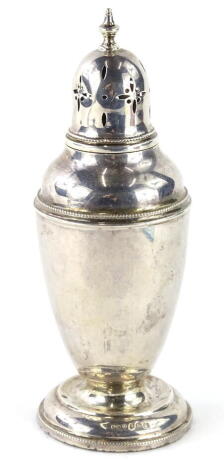 A George V silver sugar castor, with pierced domed lid, surmounted by an urn finial, the shouldered body with a bead banding, on a squat inverted stem and circular domed foot, Birmingham 1929, 18cm high, 3oz.