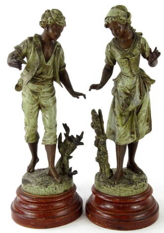 After Bruchon. A pair of early 20thC spelter figures of a boy and girl, each in flowing robes, aside tree boughs on inverted circular plinth bases, bearing signatures, 39cm high.
