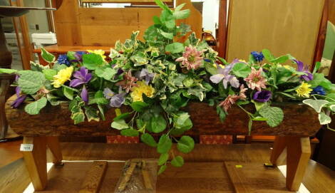 A wooden trough, in the form of a hollow tree trunk, filled with artificial flowers, 93cm wide.