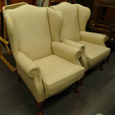 A pair of modern wing armchairs, with shaped tops, removable cushion seats and squat front cabriole legs with pad feet, in cream leather, 104cm high (2)