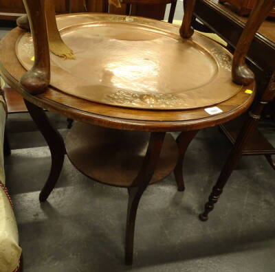 An oak two tier occasional table, the top inset with embossed and hammered copper Arts and Crafts style tray on shaped supports, 70cm diameter.