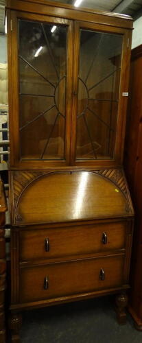 A mid 20thC oak bureau bookcase, with lead glass sunburst door, carved fall and two drawers, on shaped feet, 196cm high, 75cm wide, 49cm deep.