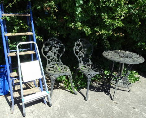 A three piece metal patio suite comprising circular table, 68cm high, 59cm diameter and two shaped chairs with rose backs and two folding step ladders.