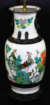 A Japanese pottery lamp vase, of shouldered circular form, polychrome decorated with exotic bird and flowers predominately in green and orange, on fixed pierced wooden base with metal mounts, 56cm high.