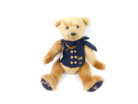 A Harrods Millennium plush jointed teddy bear 2000, with blue bow and blue jacket with gilt coloured buttons, stitched to the bottom of the feet with label, 44cm high.