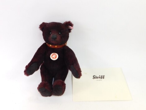 A Steiff limited edition teddy bear, in dark red, number 881/2009, with growl action and brown leather finish collar, with label to ear and paperwork, 33cm high.