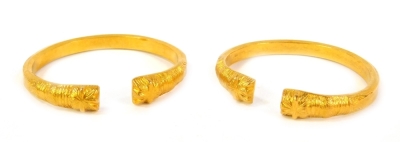 A pair of open bracelets, cast with stylised ends, unhallmarked yellow metal.