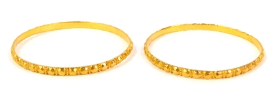 A pair of circular bangles, with faceted decoration, unhallmarked yellow metal.