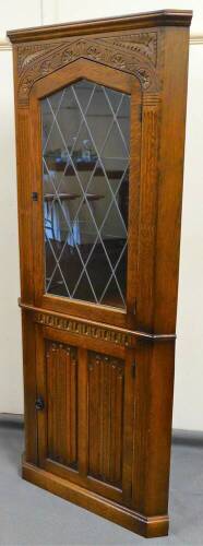 An Old Charm style oak corner cupboard, with lead glass panel door, flanked by carved fluting above a linen fold cupboard, on a block base with electrical feature, 179cm high, 70cm wide, 41cm deep.