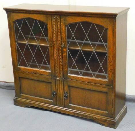 A late 20thC Old Charm style oak bookcase, with lead glass panel diamond shaped doors raised above a double cupboard on bracket feet, 97cm high, 108cm wide, 30cm deep.