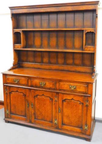 A 20thC Stanley Cumper oak dresser, the upper section with Delft racking above open cupboards with small drawers raised above three frieze drawers with plain back and swan neck handles, with triple cupboards beneath, 185cm high, 141cm wide, 52cm deep.