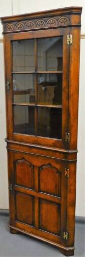 A 20thC Stanley Cumper oak freestanding corner drinks cupboard, with a carved top raised above a glazed cupboard with shaped shelves, the subsection with a four panelled cupboard door on shaped feet, 195cm high, 72cm wide, 49cm deep.