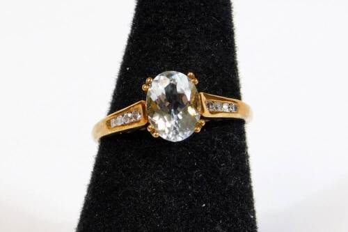 A dress ring, claw set with oval aquamarine coloured stone with small diamonds to the shoulders, on a part pierced shank, marked 9K, size N, 2.2g all in.