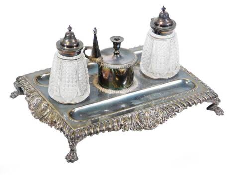 An Edwardian electroplate desk stand, in the George III style, having gadrooned and shell border, raised on paw feet, incorporating two cut crystal ink wells and central taper stick with snuffer, 28cm wide.