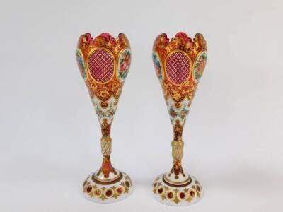 A pair of late 19thC Bohemian flashed cranberry glass vases, of ogee form, raised on a slender collared stem, reserve painted with flowers, against a white ground, with gilt foliate decoration against the cranberry glass, 26.5cm H. (AF) - 2