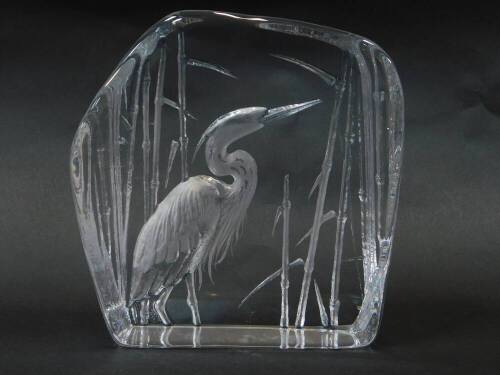 A Mats Jonasson intaglio glass sculpture of a heron, modelled standing against bulrushes, etched signature, 18cm wide, 18cm high.