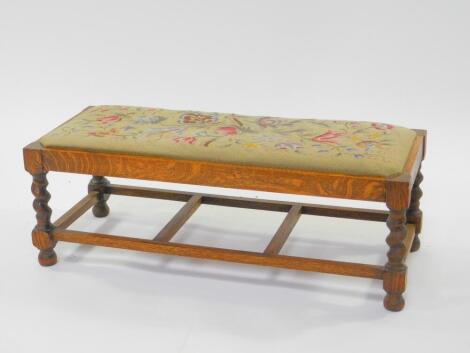 An early 20thC oak duet stool, with a floral wool work tapestry seat, raised on spiral twist columns, united with by a box stretcher, 31cm High, 86cm Wide, 35cm Deep.